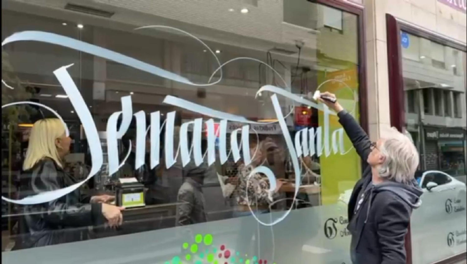 Miguel Guerrero escribiendo con tiza líquida la frase Semana Santa con letra anchas y góticas en escaparate