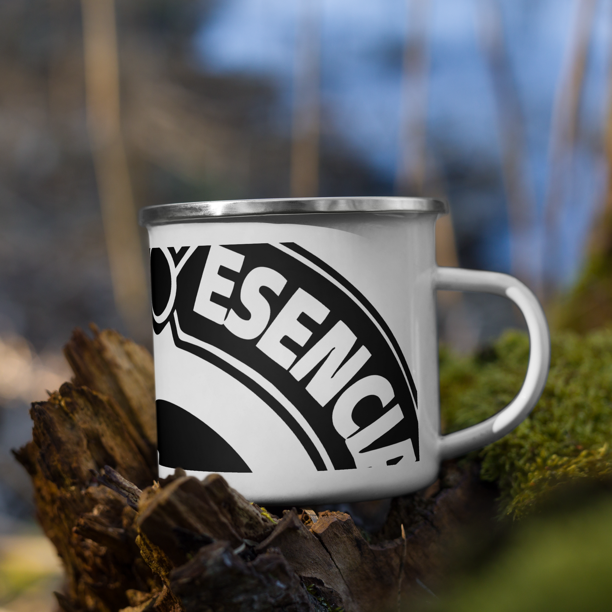 taza esmaltada de color blanco con el logo de la marca registrada tinta esencia impreso en negro. sobre un tronco de madera i musgo